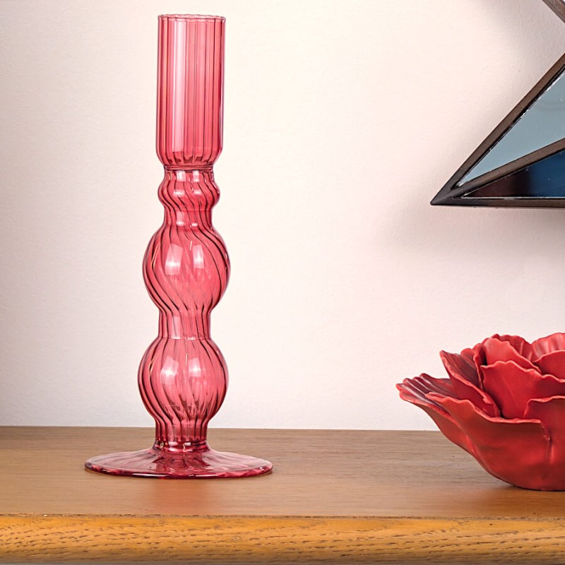 Bougeoir en verre rose framboise posé sur un meuble en bois à côté d'une fleur en porcelaine bordeaux.