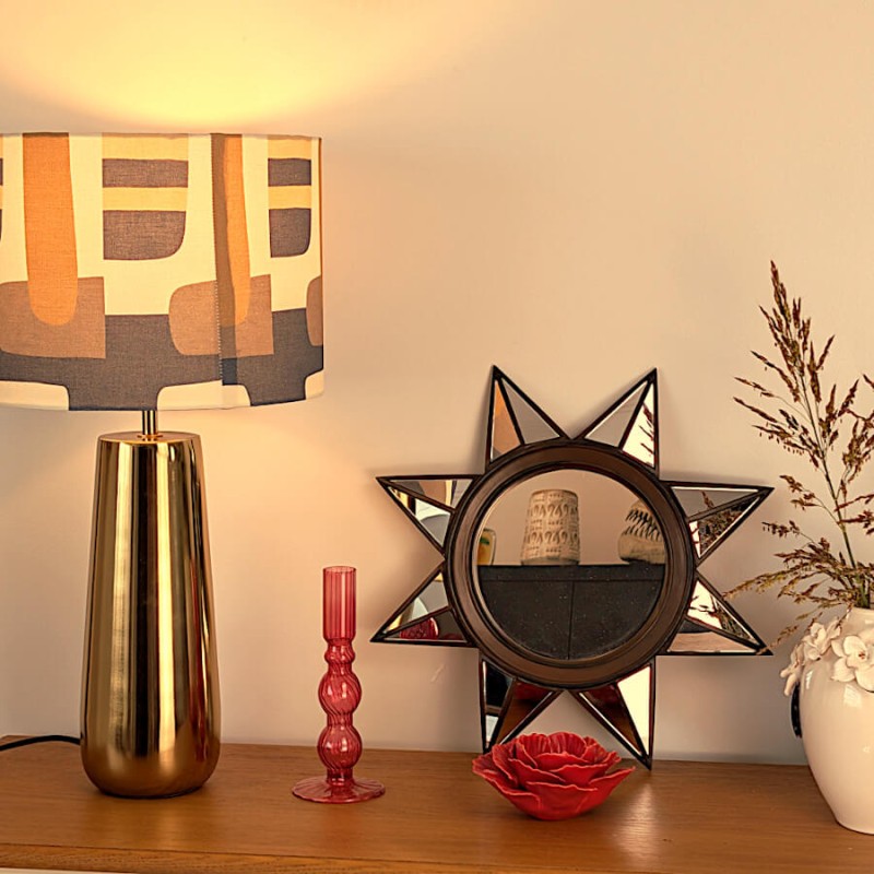 Vue d'ensemble d'un buffet déco avec lampe dorée style 70s, miroir soleil et bougeoir rose.