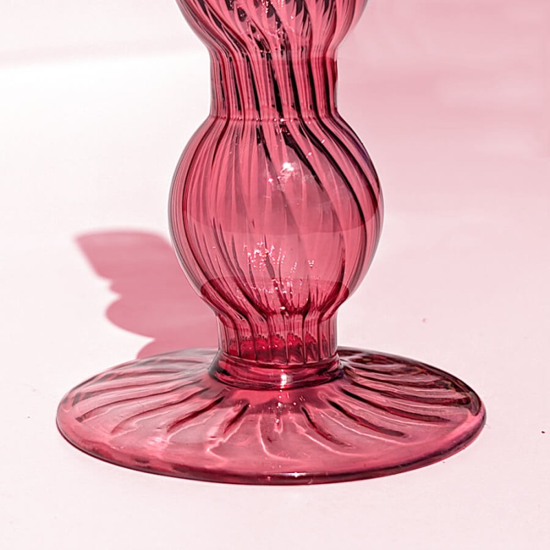 Gros plan sur le pied évasé et sculpté en verre rose teinté.