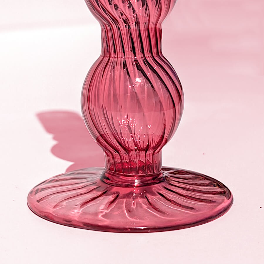 Gros plan sur le pied évasé et sculpté en verre rose teinté.