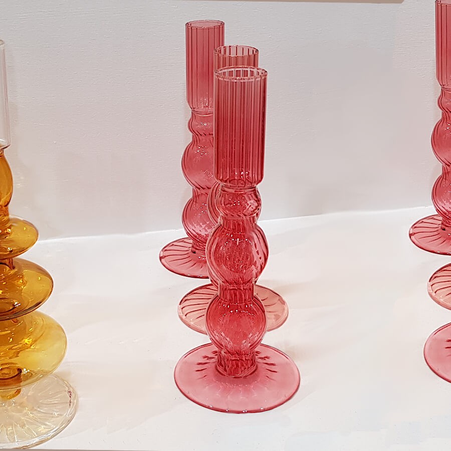 Présentation en alignement de plusieurs bougeoirs en verre teinté rose.